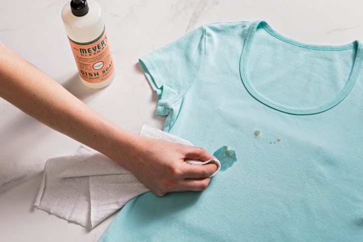 Secando una mancha de grasa en una camiseta azul, con jabón para platos y un paño